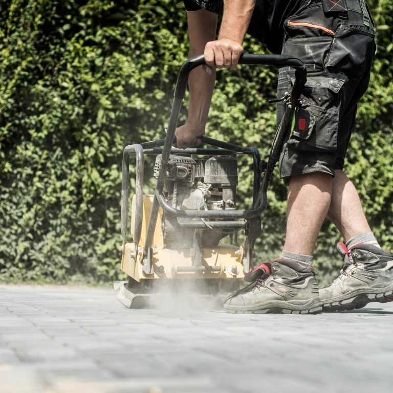Arbeiter fährt mit einer Rüttelplatte über die frisch verlegten Pflastersteine in der neuen Einfahrt