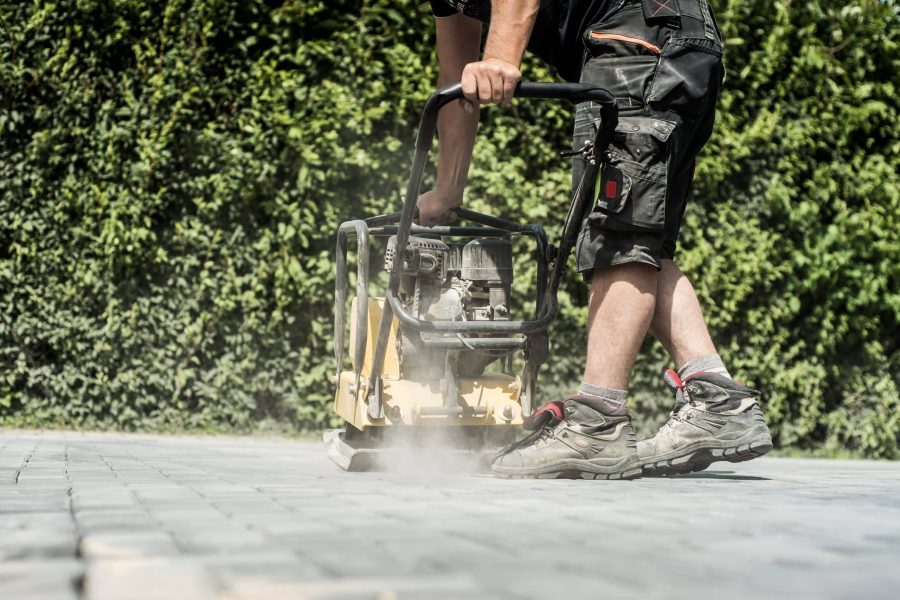 Arbeiter fährt mit einer Rüttelplatte über die frisch verlegten Pflastersteine in der neuen Einfahrt