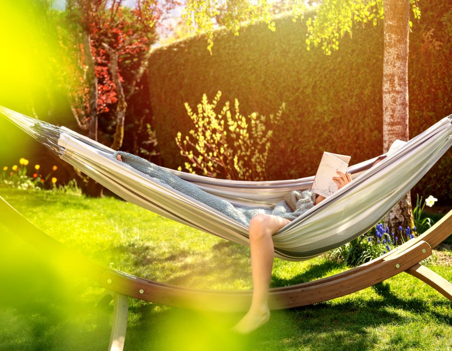 Young relaxed girl reading book in hammock in garden at home at bright sunset. Slow living, gadget detox and weekend leisure activity. Quarantine and self isolation period Young relaxed girl reading book in hammock in garden at home at bright sunset. Slow living, gadget detox and weekend leisure activity. Quarantine and self isolation period